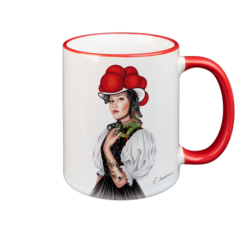 A white ceramic mug with a red handle features an illustration of a woman. The woman is wearing traditional attire, including a red hat adorned with large pom-poms, a colorful embroidered neckpiece, and a white blouse. Microwave and dishwasher safe, there's also a signature near the bottom right. Presenting the MUG – Bollenhut Black Forest Bonnie by Cuckoo's Nest.